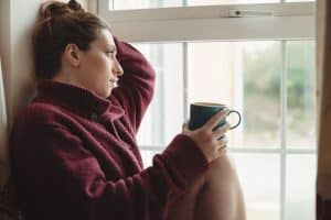 Mulher branca olhando a janela sentindo os efeitos da cafeína e ansiedade