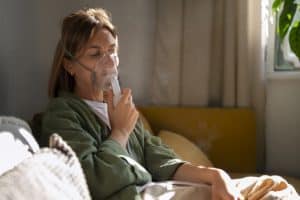 asma-o-que-fazer-mulher-branca-sentada-no-sofá-usa-nebulizador-para-tratar-crise-de-asma