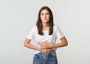 Mulher branca com expressão de desconforto, segurando a mão sobre a região abdominal, indicando síndrome nefrótica