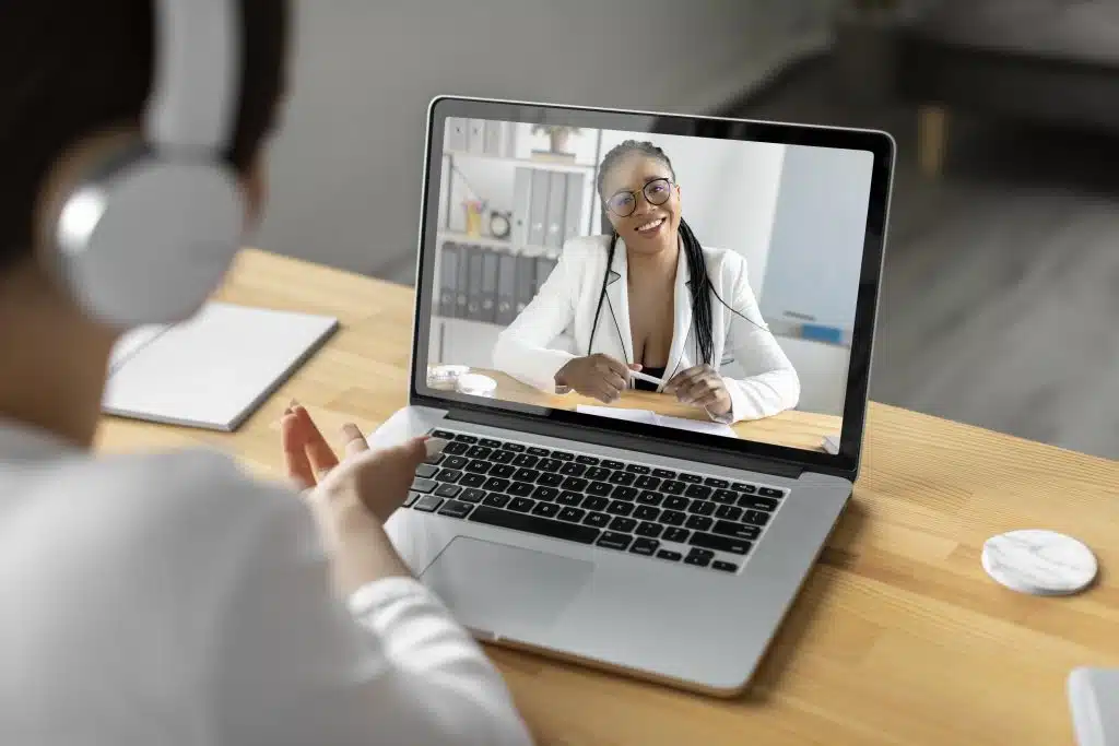 Paciente em consulta por telemedicina, conversando com uma profissional de saúde por vídeo chamada no notebook, ilustrando o uso da saúde digital e do atendimento médico remoto