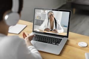 Paciente em consulta por telemedicina, conversando com uma profissional de saúde por vídeo chamada no notebook, ilustrando o uso da saúde digital e do atendimento médico remoto