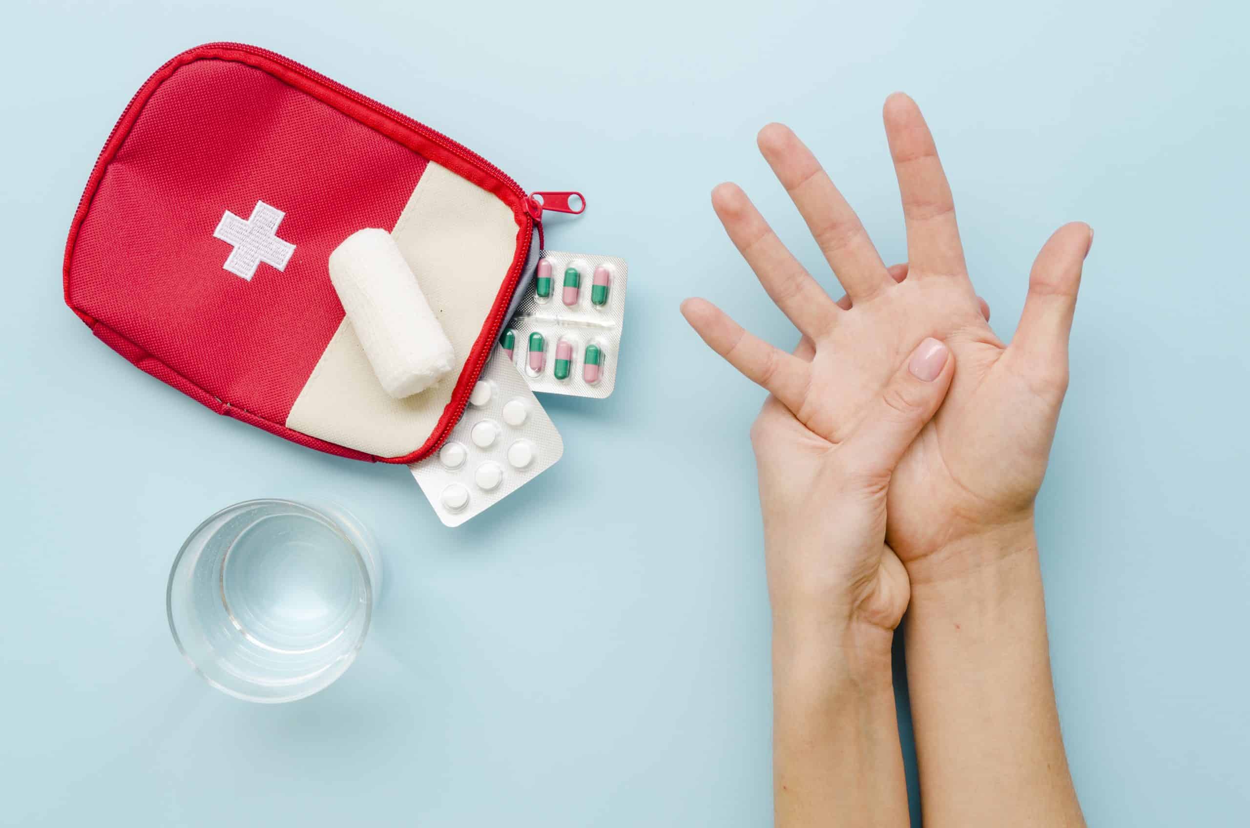 Kit de primeiros socorros com curativos, comprimidos e água ao lado de uma pessoa segurando a própria mão, ilustrando cuidados básicos em situações de emergência do dia a dia