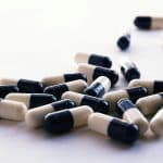 Cápsulas de medicamento espalhadas sobre uma superfície branca, representando o uso da Losartana no tratamento da pressão alta e seus possíveis efeitos no organismo