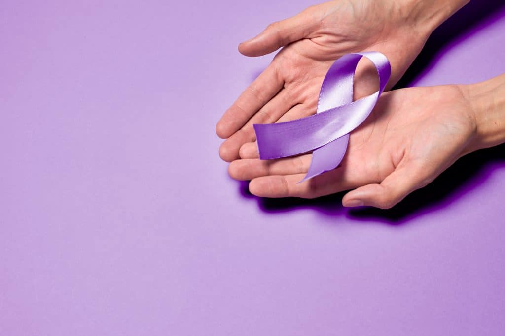 Mãos segurando um laço roxo em campanha de conscientização da hanseníase