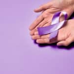 Mãos segurando um laço roxo em campanha de conscientização da hanseníase