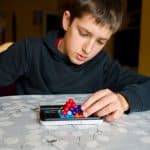 Criança concentrada manipulando um jogo de bolinhas coloridas sobre a mesa, representando desafios de atenção e foco associados ao TDAH.