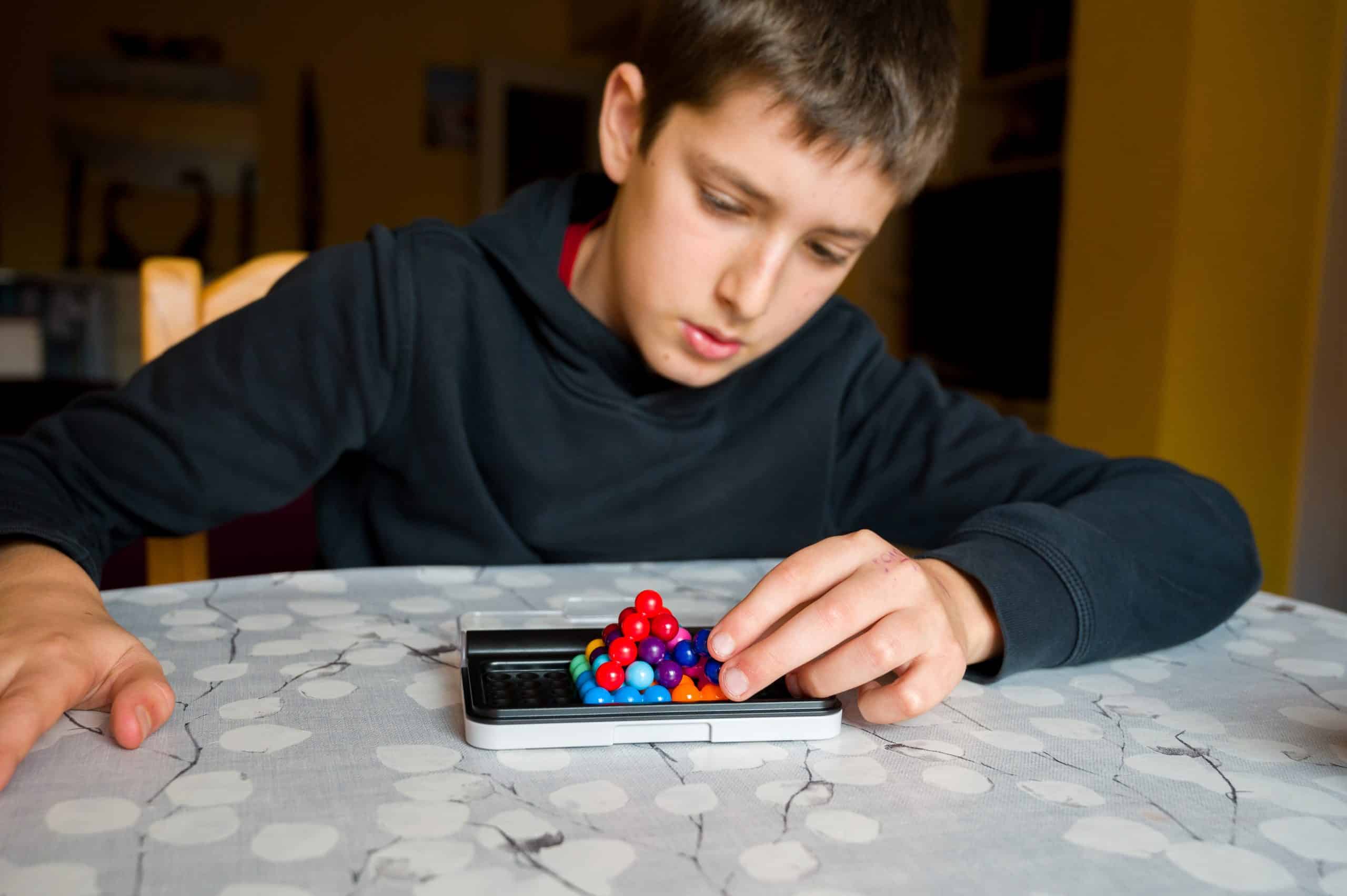Criança concentrada manipulando um jogo de bolinhas coloridas sobre a mesa, representando desafios de atenção e foco associados ao TDAH.
