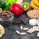 Alimentos ricos em magnésio, como abacate, banana, sementes, cacau, feijão e vegetais, ao lado de cápsulas de suplemento sobre a mesa.