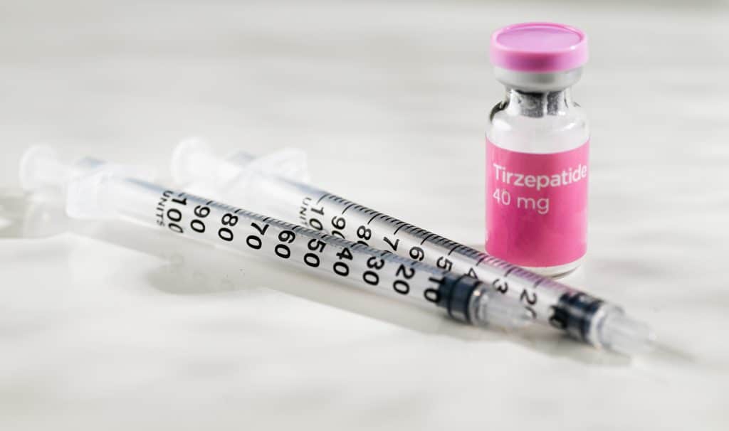 Frasco de tirzepatida 40 mg ao lado de seringas graduadas, sobre fundo claro, representando medicamento injetável de uso controlado.