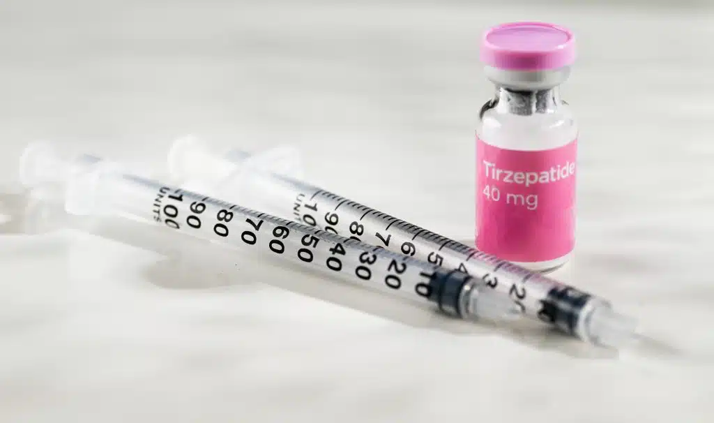 Frasco de tirzepatida 40 mg ao lado de seringas graduadas, sobre fundo claro, representando medicamento injetável de uso controlado.