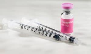 Frasco de tirzepatida 40 mg ao lado de seringas graduadas, sobre fundo claro, representando medicamento injetável de uso controlado.