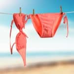 Biquíni rosa pendurado para secar ao ar livre, ilustrando cuidados simples após praia ou piscina para prevenir candidíase de repetição.
