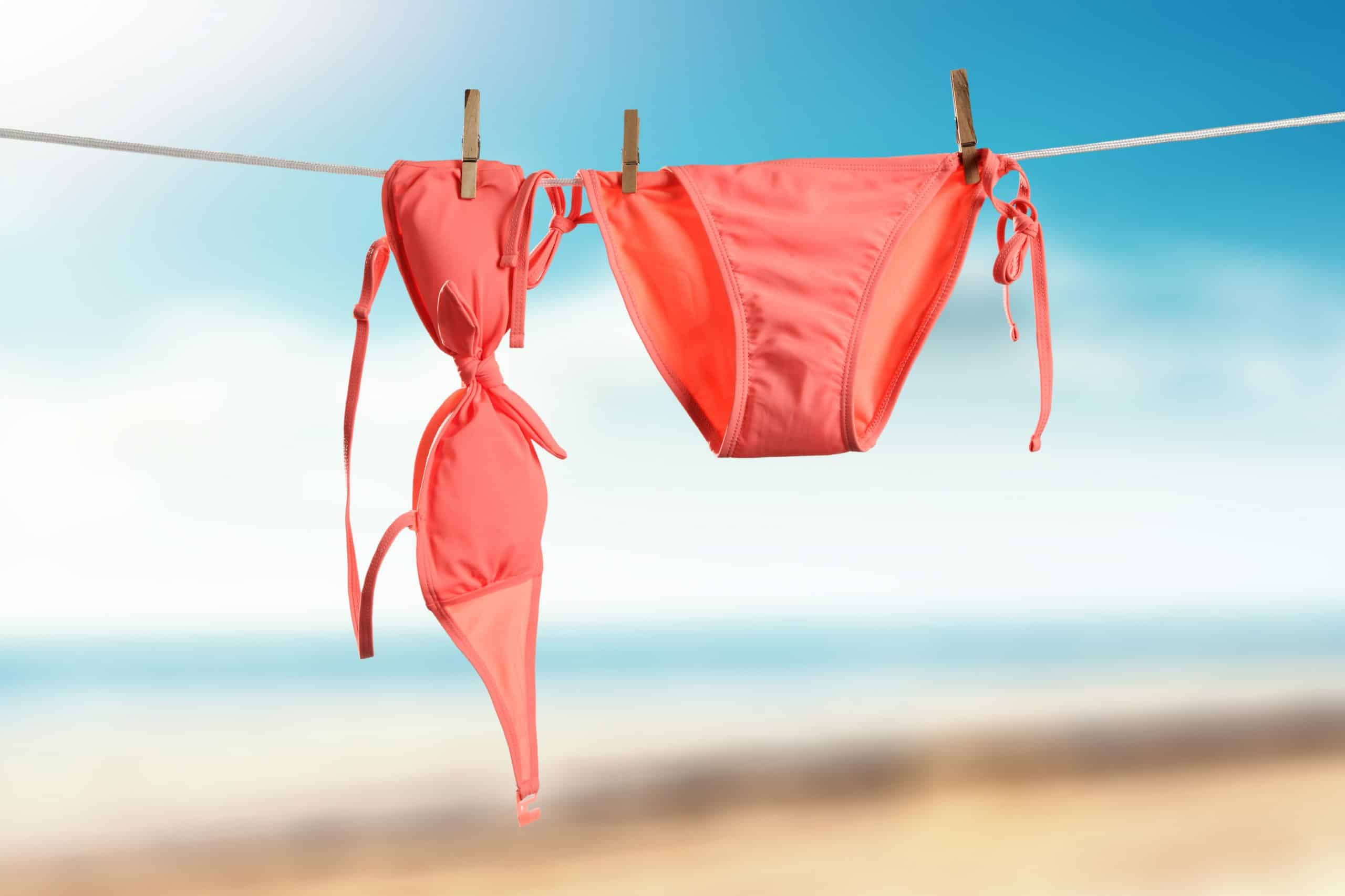 Biquíni rosa pendurado para secar ao ar livre, ilustrando cuidados simples após praia ou piscina para prevenir candidíase de repetição.