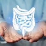 Mãos abertas sustentando uma ilustração do intestino humano em destaque, representando informações sobre câncer colorretal, seus sintomas, causas e tratamento.