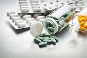 Frascos abertos e cartelas com comprimidos e cápsulas sobre a mesa, ilustrando diferentes formas de uso de medicamentos, incluindo medicamento sublingual e via oral.