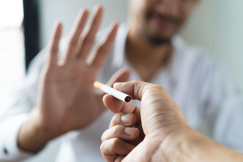 Pessoa recusa um cigarro oferecido por outra mão, representando a decisão de abandonar o tabagismo e os caminhos de tratamento para quem busca saber como parar de fumar.