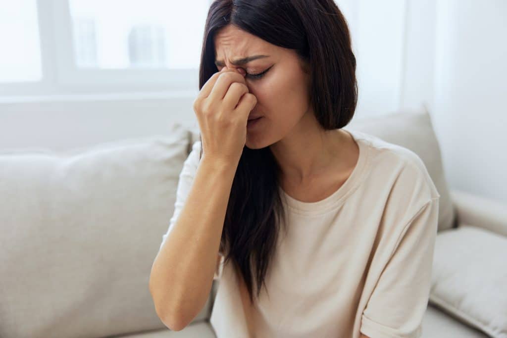 Mulher com expressão de dor pressionando a região do nariz e dos olhos, ilustrando sintomas comuns da Sinusite, como pressão facial e desconforto nasal.