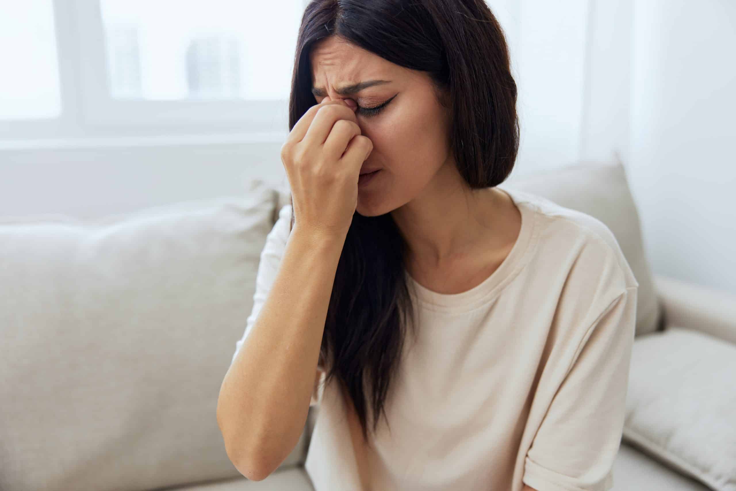 Mulher com expressão de dor pressionando a região do nariz e dos olhos, ilustrando sintomas comuns da Sinusite, como pressão facial e desconforto nasal.