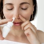 Mulher utilizando descongestionante nasal em spray para aliviar a congestão, representando os cuidados necessários com o uso desse tipo de medicamento.