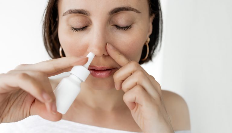 Mulher utilizando descongestionante nasal em spray para aliviar a congestão, representando os cuidados necessários com o uso desse tipo de medicamento.