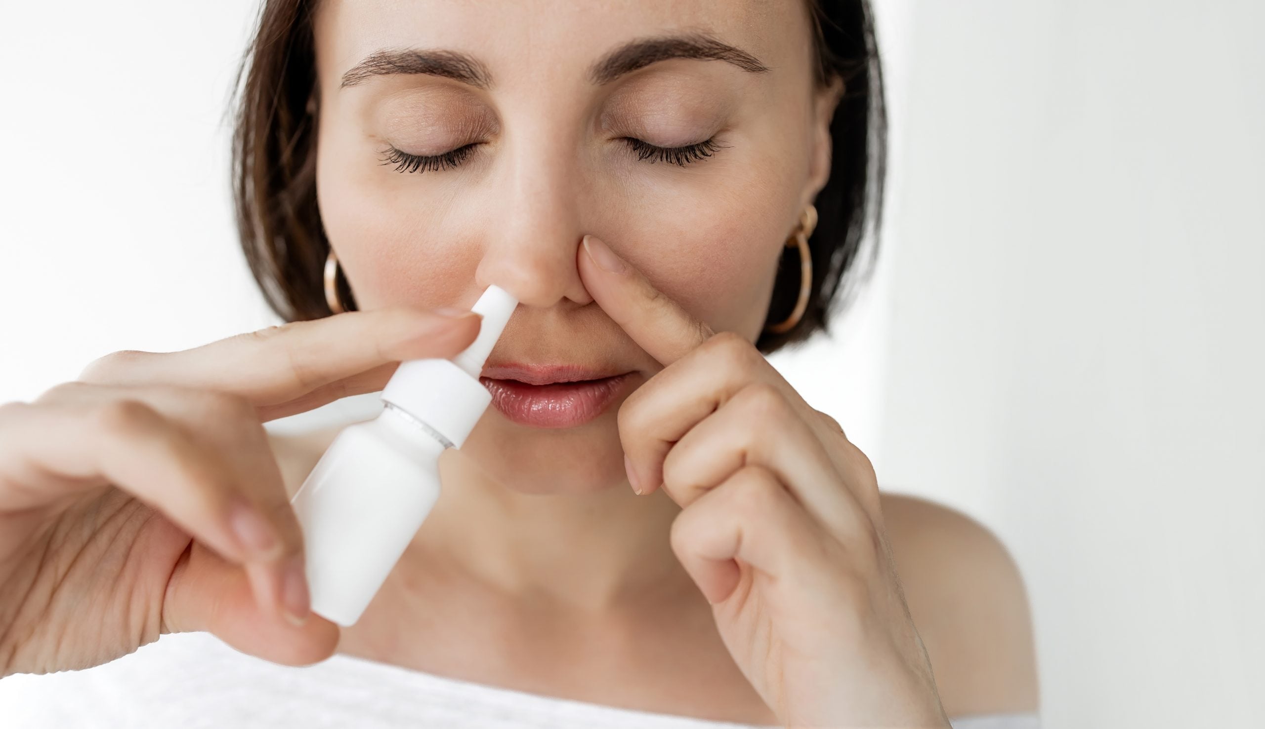 Mulher utilizando descongestionante nasal em spray para aliviar a congestão, representando os cuidados necessários com o uso desse tipo de medicamento.