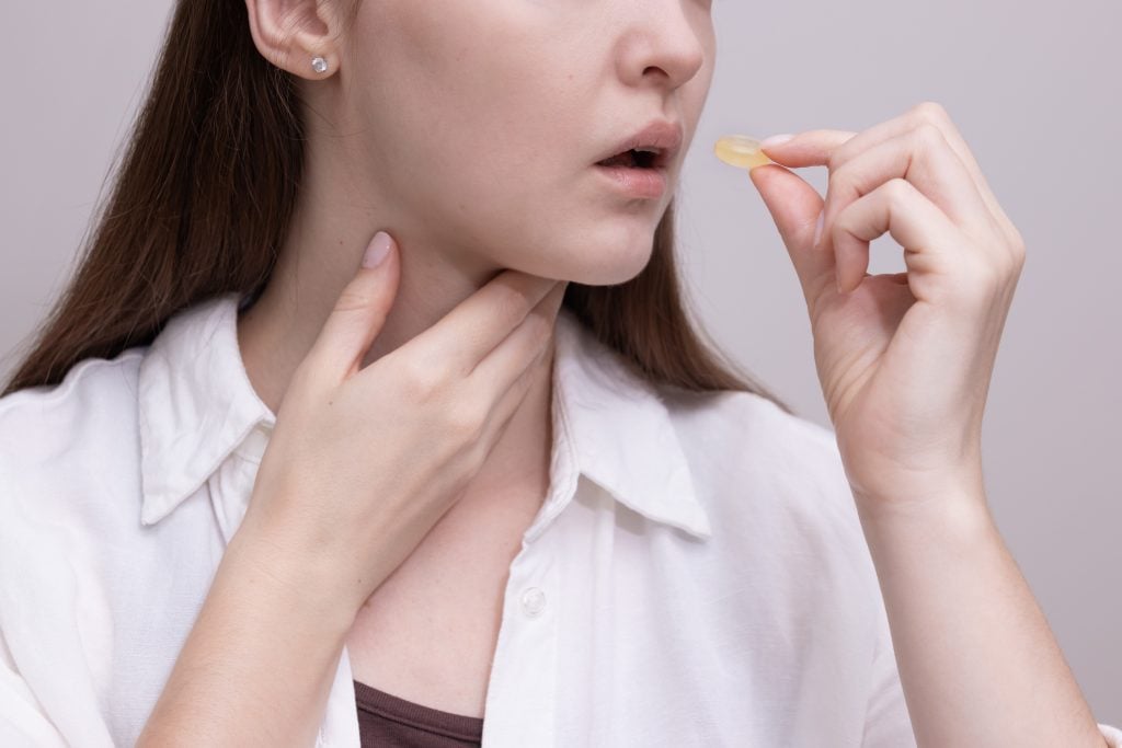 Pastilhas para garganta: Mulher segurando uma pastilha próxima à boca e tocando o pescoço, representando o uso de pastilhas para aliviar desconfortos e irritações na garganta.