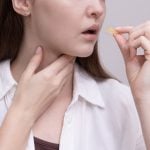 Pastilhas para garganta: Mulher segurando uma pastilha próxima à boca e tocando o pescoço, representando o uso de pastilhas para aliviar desconfortos e irritações na garganta.